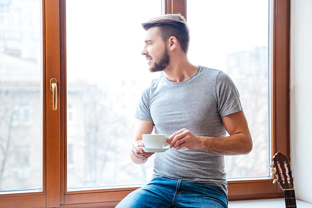 anaheimlighthouse-how-can-i-not-regret-my-past-article-photo-handsome-young-man-sitting-on-windowsill-and-drinking-coffe-404988769