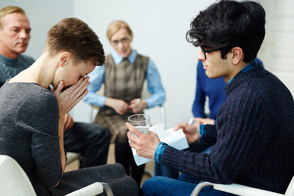anaheimlighthouse-will-i-always-be-an-addict-article-photo-young-man-giving-glass-of-water-to-groupmate-during-psychological-session-583810342