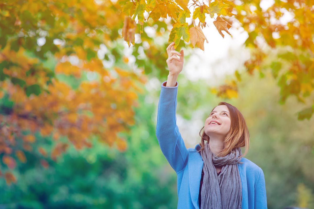 anaheimlighthouse-how-to-stay-sober-over-thanksgiving-if-youre-alone-article-photo-young-redhead-woman-in-blue-coat-holding-yellow-maple-tree-leaf-in-autumn-park-735895759