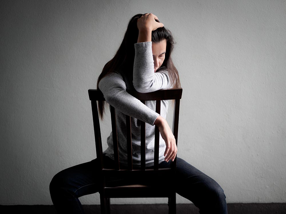 anaheimlighthouse-why-do-people-stay-in-abusive-relationships-article-photo-depressed-broken-hearted-woman-sitting-alone-on-a-wooden-chair-in-dark-room-at-home-lonly-sad-1034300851
