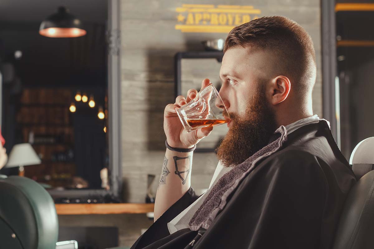 anaheimlighthouse-do-people-actually-tell-the-truth-when-drunk-article-photo-serious-young-bearded-man-sitting-in-chair-at-barbershop-and-drinking-whiskey-from-a-glass-401201932