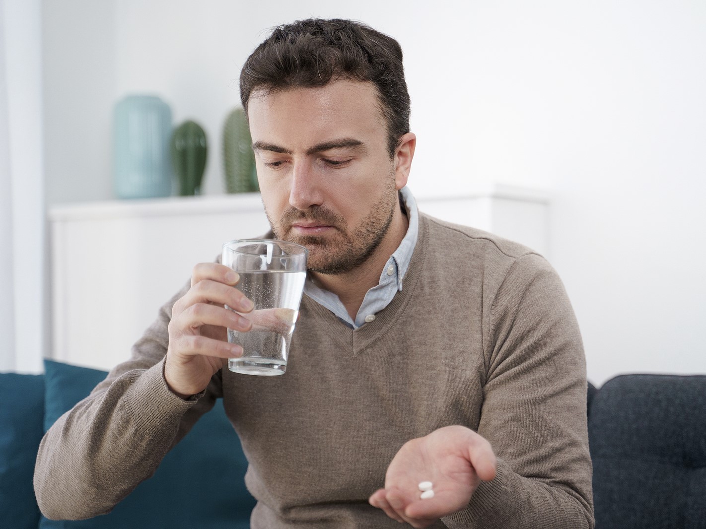 A man holding two gabapentin pills on his palm and a glass of water on the other hand