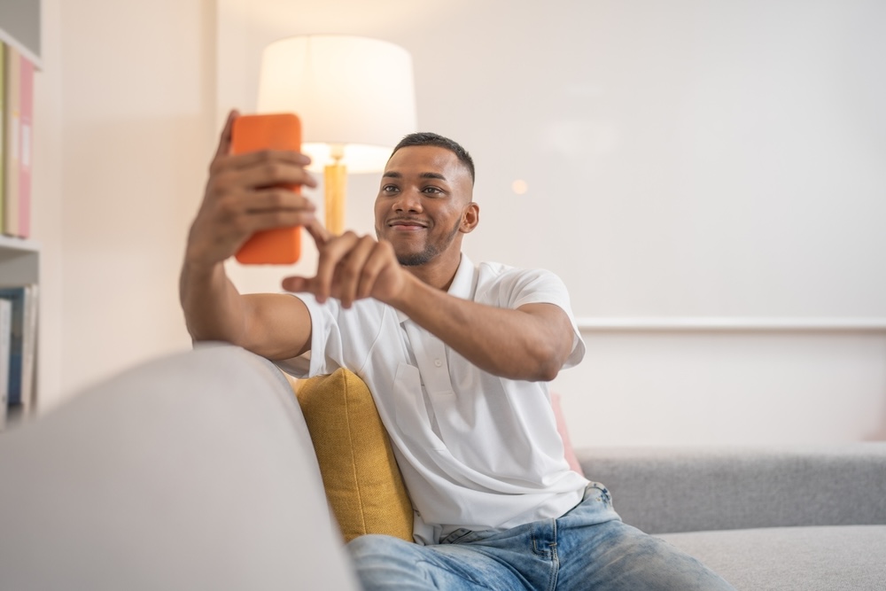 A man in a white shirt looking at his orange phone writing Thanksgiving messages 