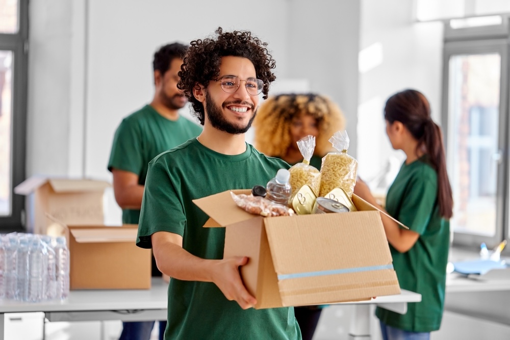 A man in a green shirt carries a box of food as he volunteers in a local food bank