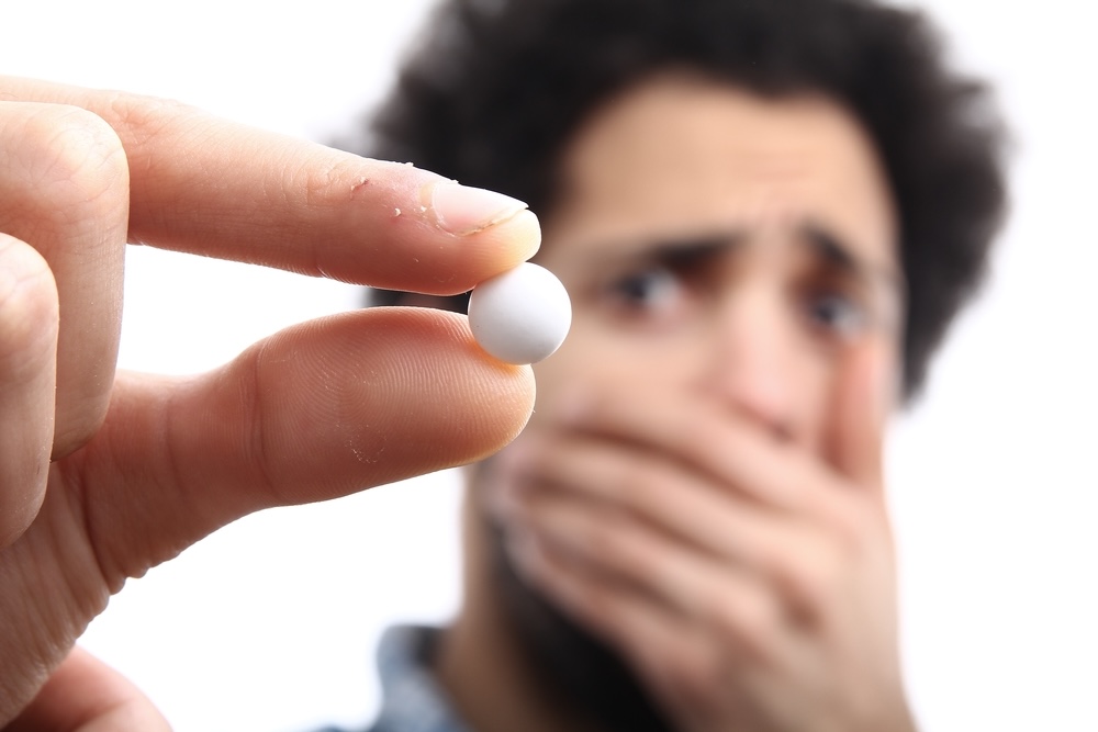 A man covering his mouth holds out a white pill 