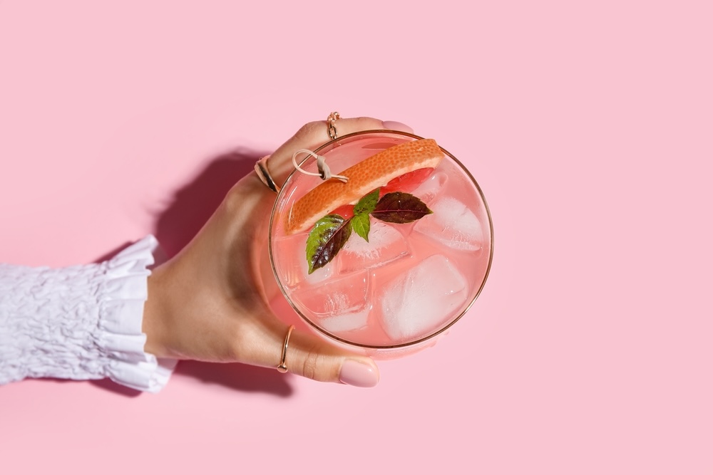 Woman holding glass of pink whitney vodka on pink color background.