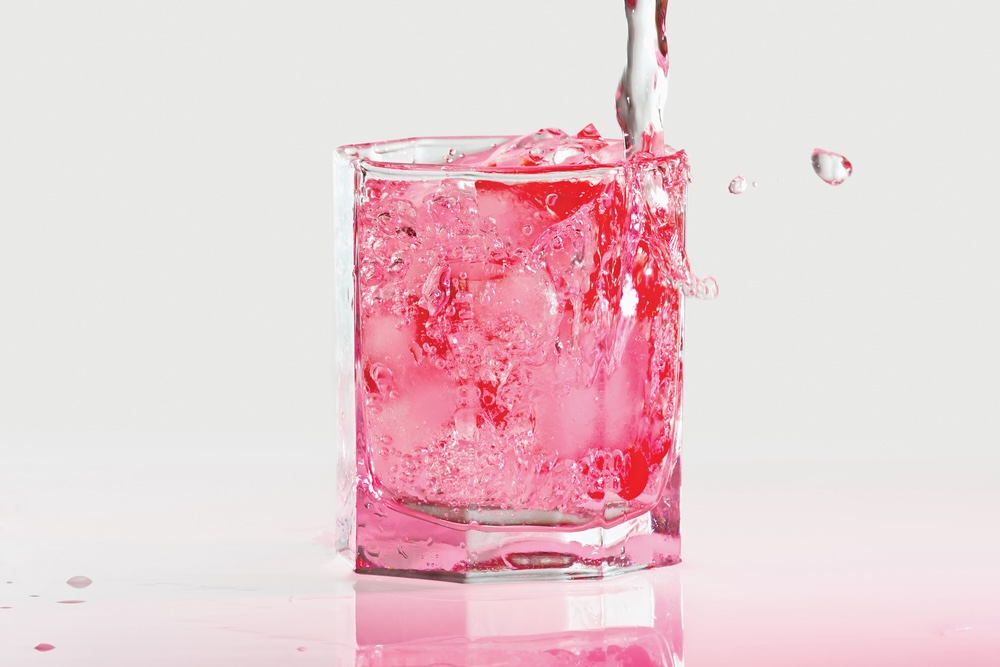 A glass of pink whitney vodka with splash in pink light