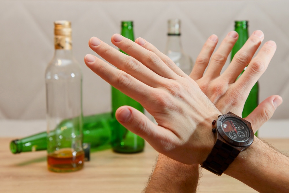 Hands of a man with black watch in front of bottles of alcohol