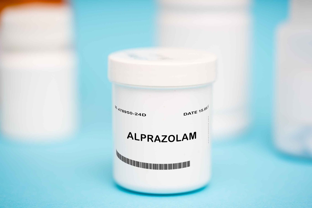 White plastic bottles of alprazolam pills on a blue surface