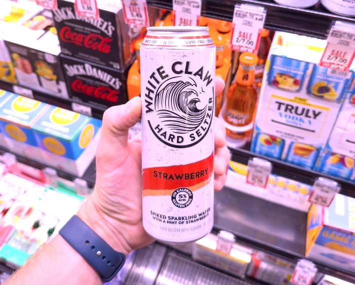 Closeup of hand holding a can of Strawberry White Claw inside a supermarket