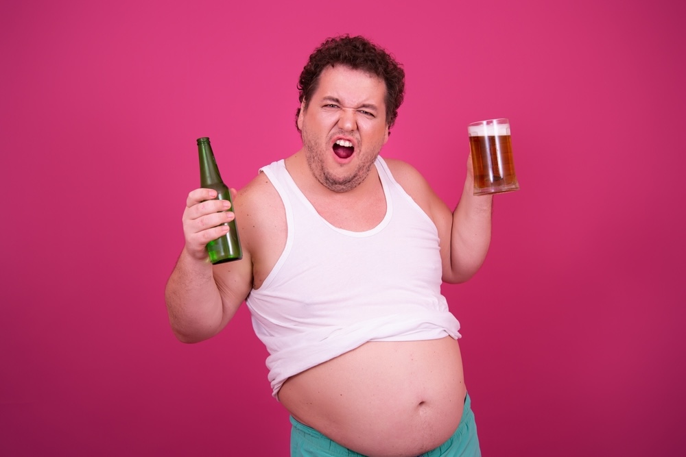 Man with a beer belly holding a beer bottle and a mug of beer 