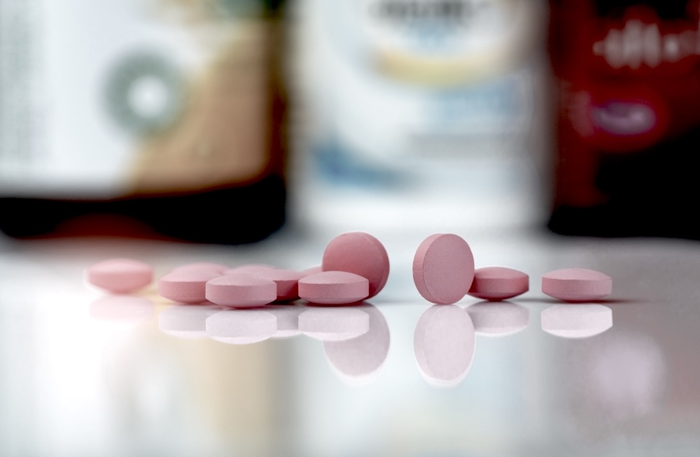 Pink painkillers on a reflective surface with medicine bottles in the background