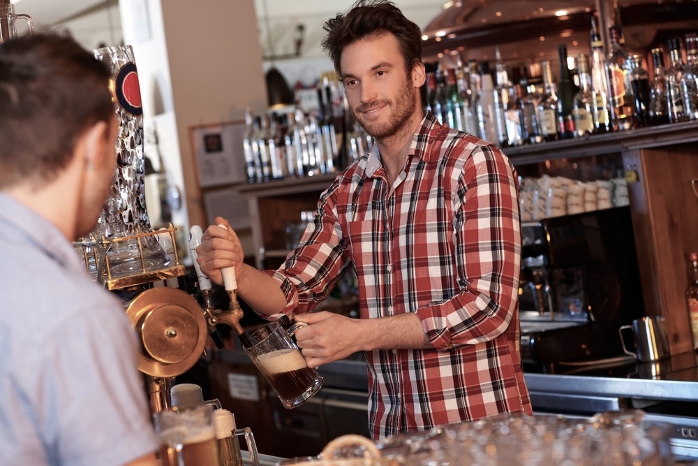 Bartender in plaid shirt serving a customer draft beer