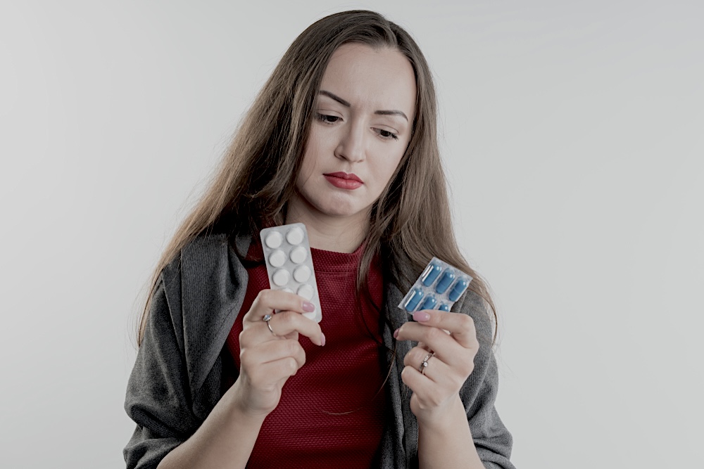 Woman holding to packets of medicines in her hands with a confused look on her face 