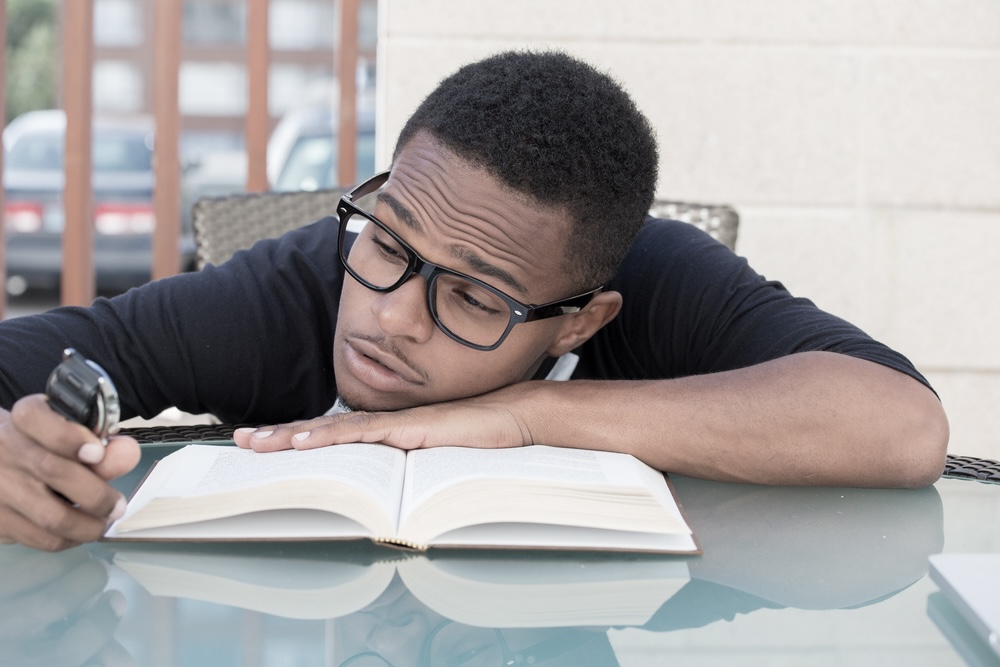 Male student slumped on a book trying to concentrate 