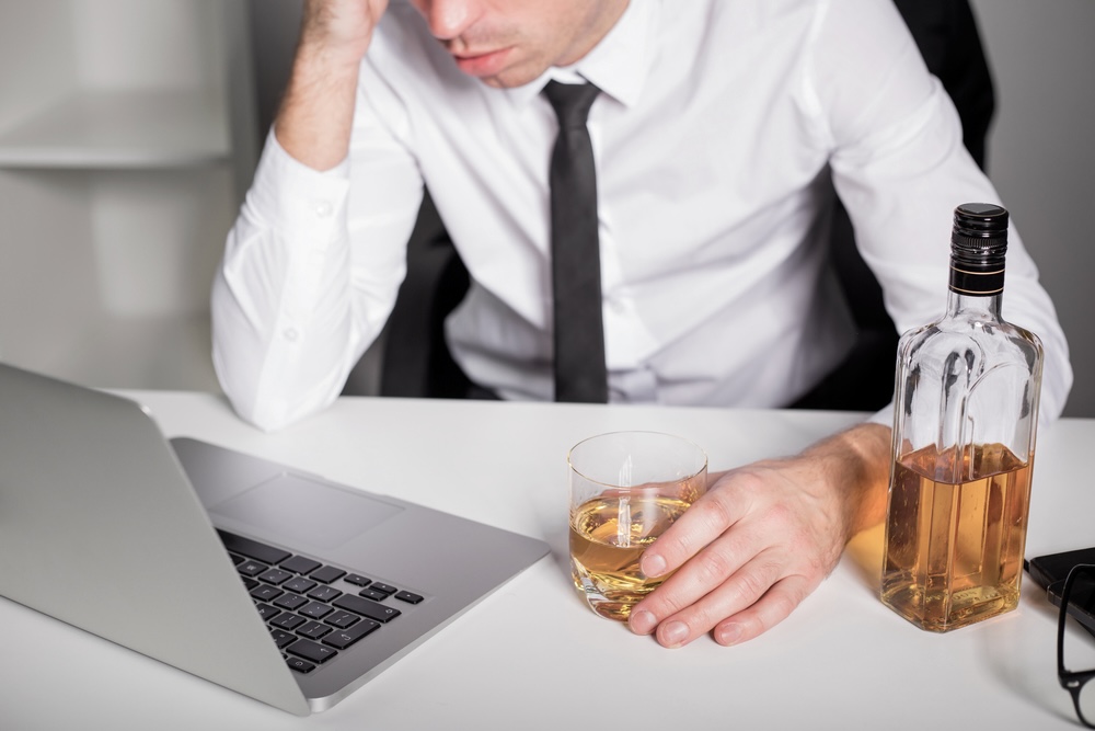 Man in the office drinking while reading from his laptop