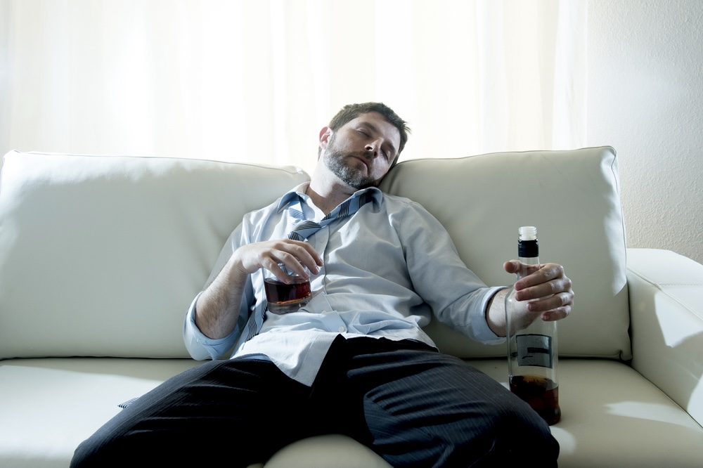 Office employee drunk on the couch holding an alcohol bottle