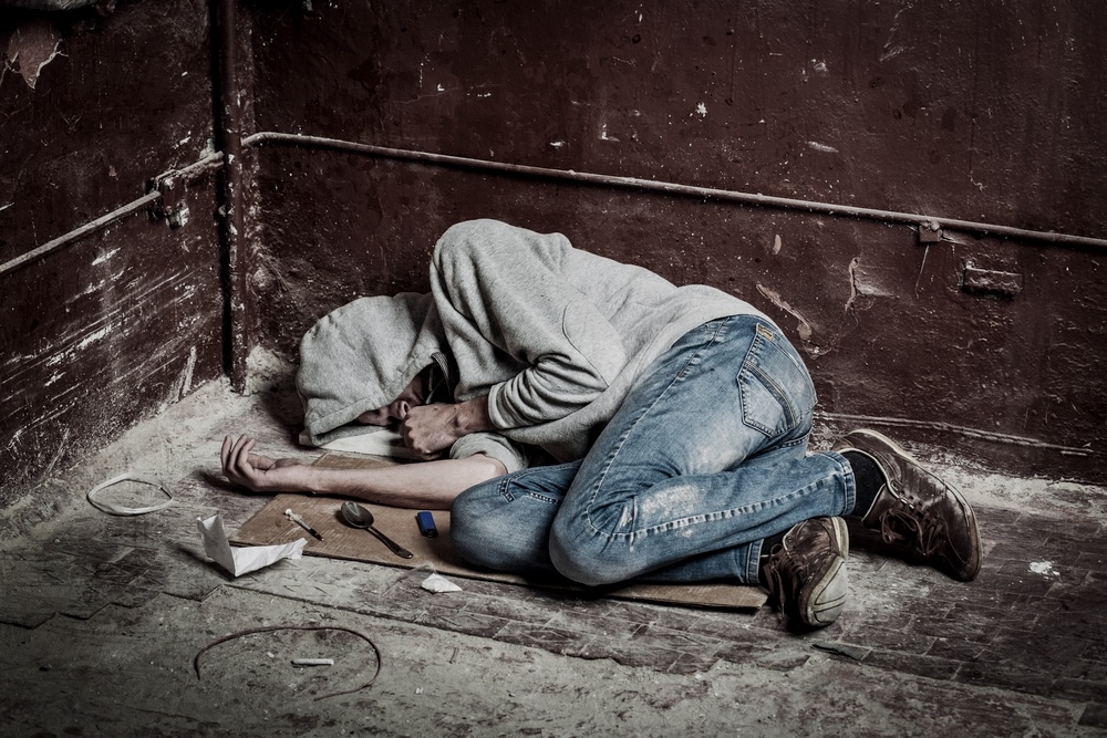 Male curled up in a corner surrounded by cocaine paraphernalia