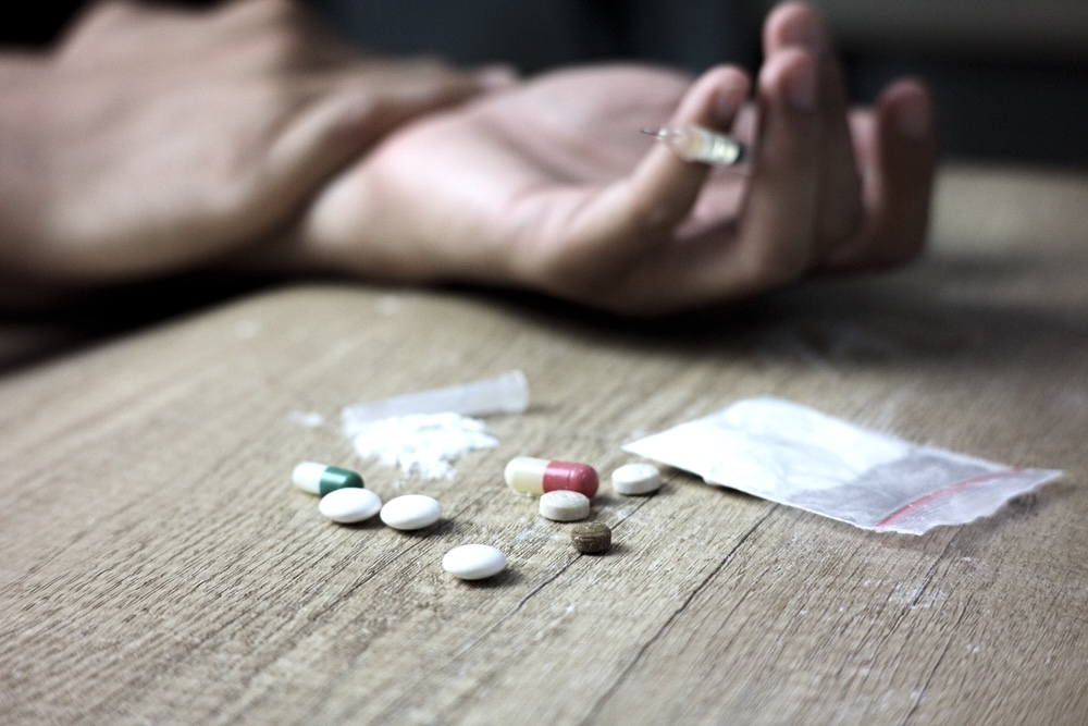 Hand of a person surrounded by a small bag of cocaine and illegal pills