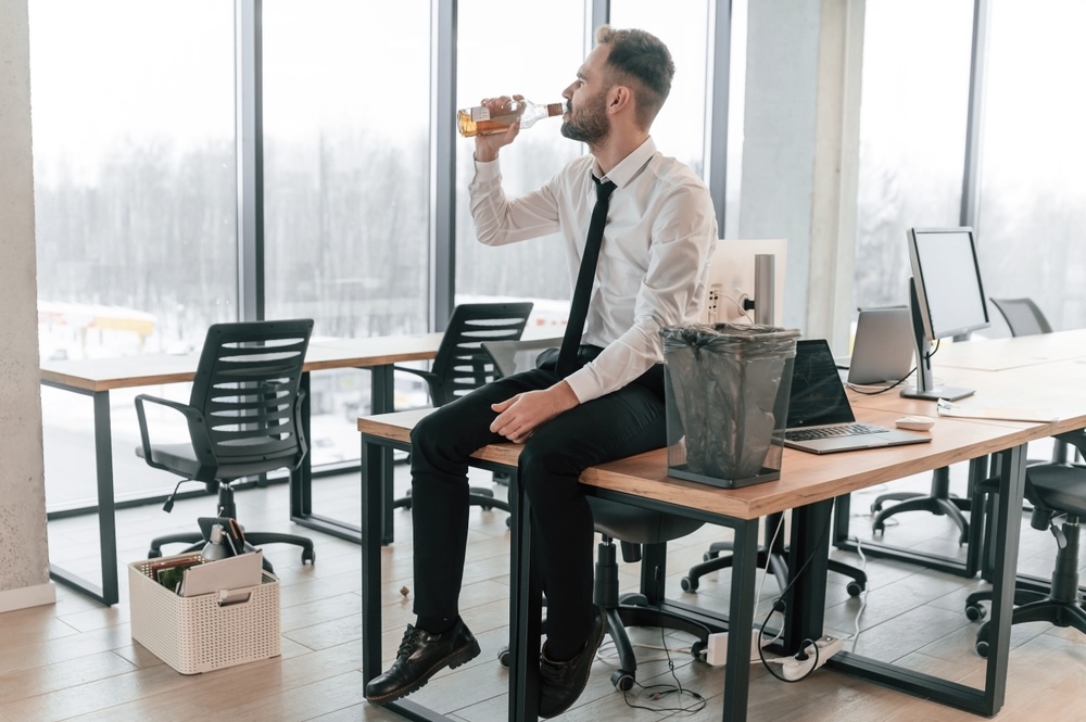 Office worker sitting on a table while drinking alcohol