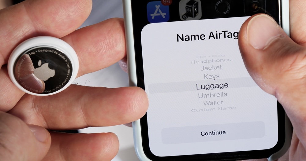 Close-up of a man’s hand settings up luggage air tag on his phone