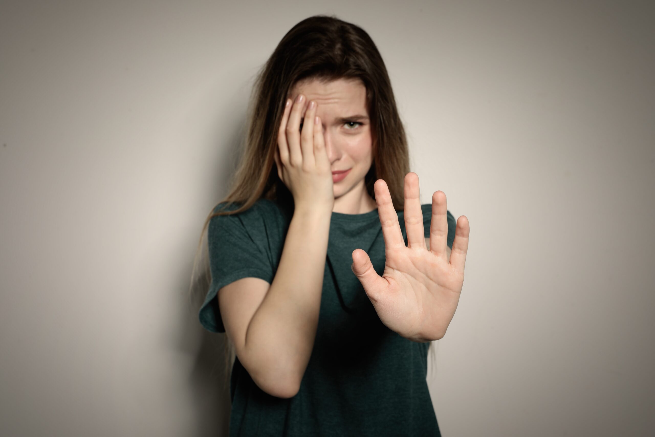 Woman covers her face with one hand, while holding out her palm to say no