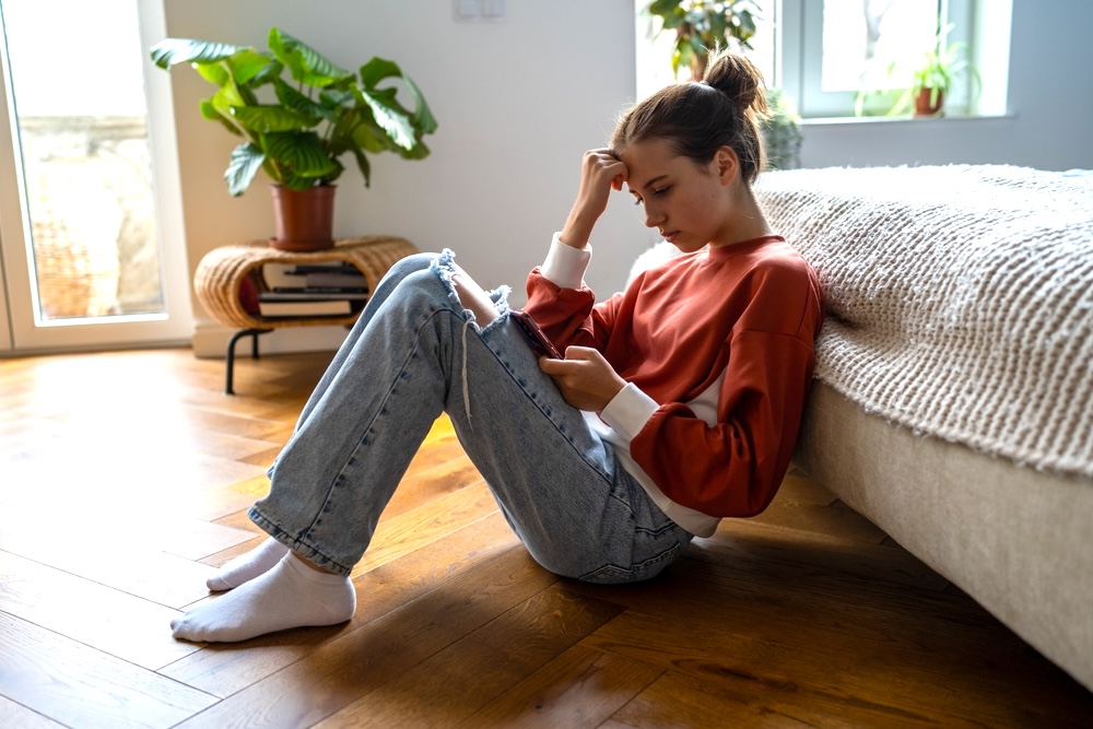 Teen sitting by her bed looking at her social media feed on her phone