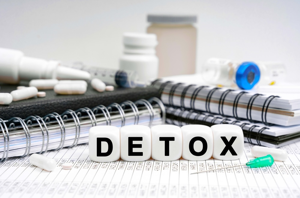 The word detox spelled out in plastic block on a desk surrounded by notebooks and pills