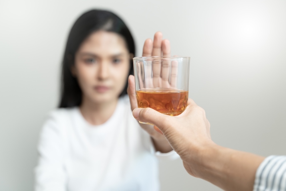 Young woman wearing white refusing a drink of alcohol 