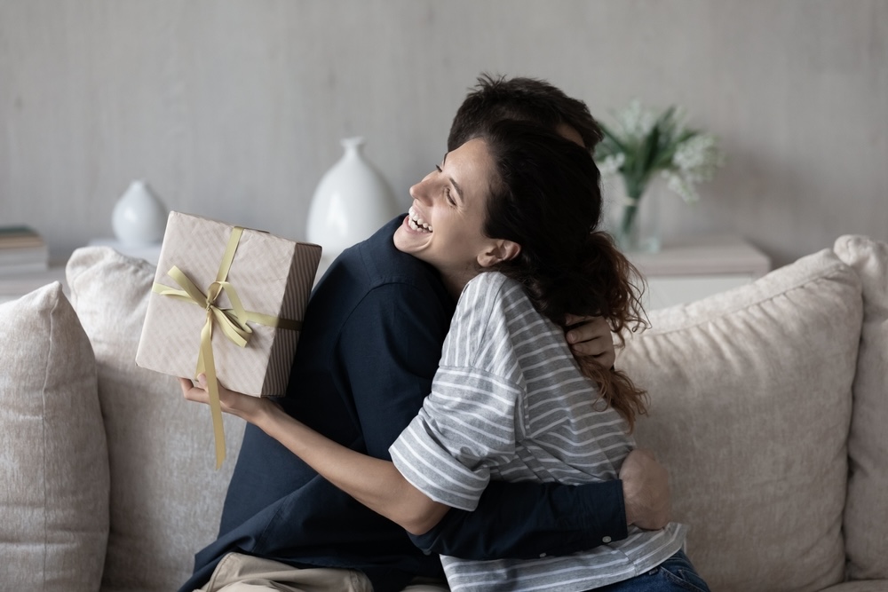 Woman congratulating her husband on sobriety anniversary holding a gift 